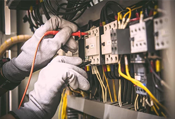 gloved hands holding a probe testing an electrical panel.